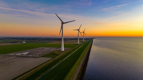 Wind turbines in the green field by sea along the beautiful coastline during sunset