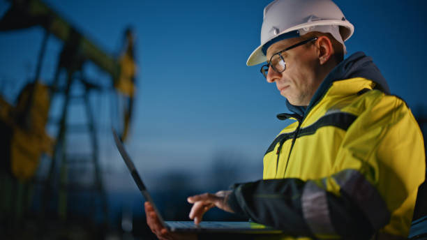istock Serious engineer using laptop while working at oil field against sky during dusk 1609593827