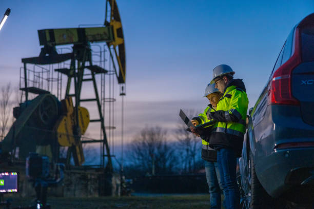 istock Engineers discussing strategy over laptop while standing by car at oil industry 1609594410