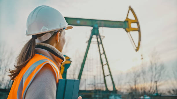 istock Female engineer with tablet PC looking at oil pump against sky 1609594414