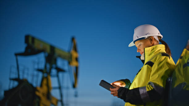 istock Female worker using tablet PC while standing by car at oil field against sky 1609594425