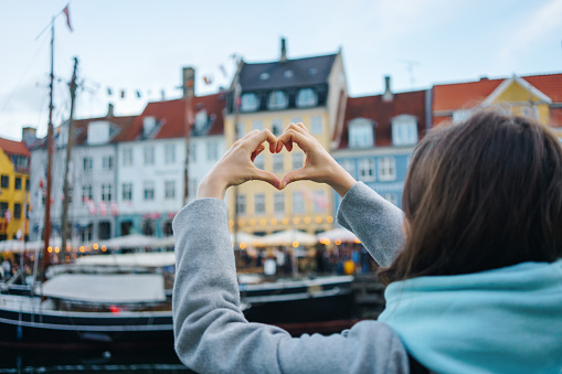 Young woman makes a heart with her hands in Nyhavn, Copenhagen, Denmark.