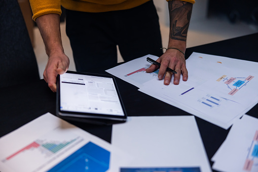 Midsection of male entrepreneur with paper documents and digital tablet working on desk at workplace