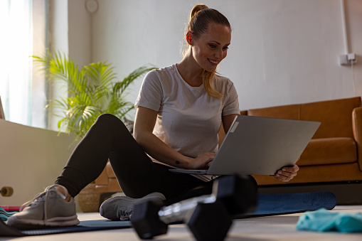 Smiling young woman using laptop after workout in living room at home