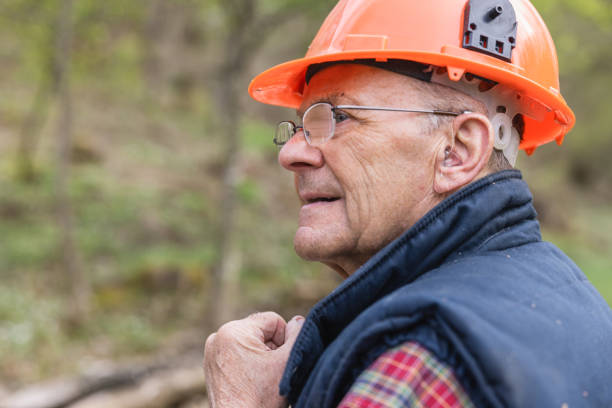 Close-up of senior lumberjack wearing hearing aid looking away at forest stock photo
