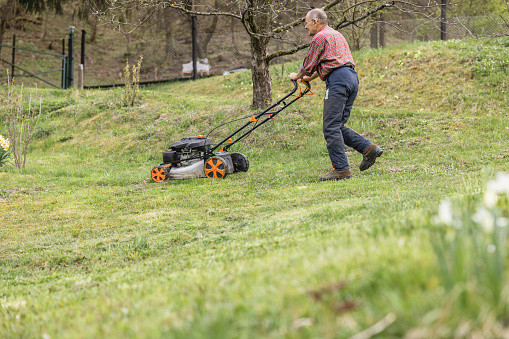 Full length of senior man wearing casuals mowing grass with lawnmower on field in yard during winter