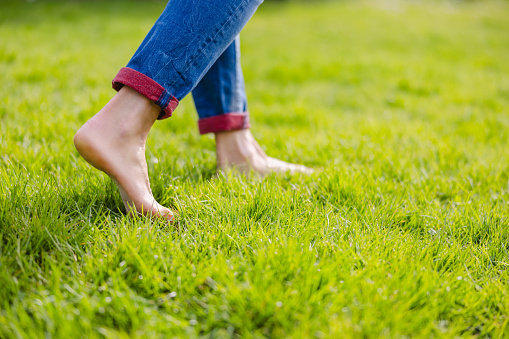 Low section of woman wearing jeans with barefoot walking on grassy field at park
