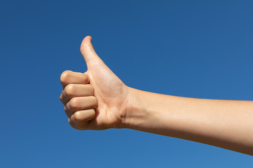 The child shows a thumbs up gesture against the blue sky, a concept on the theme of clear sunny weather