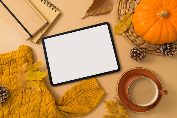istock Autumn season concept with digital tablet mock up, coffee cup, warm sweater, fall leaves and pumpkin on beige background. Top view, flat lay 1609617543