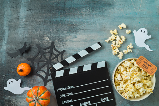 Horror movie night and Halloween party concept with  popcorn, pumpkin and movie clapper board on dark background. Top view, flat lay