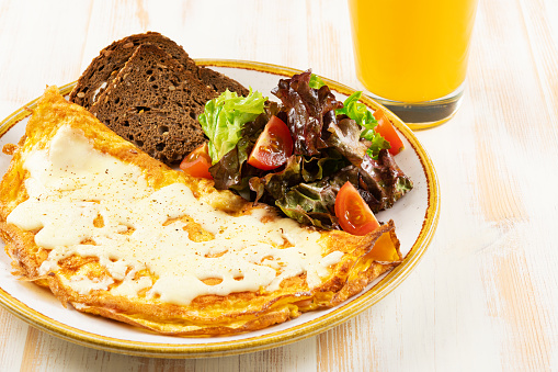 Omelette with cheese, tomatoes and green with orange juce on wooden background. Tasty freshly breakfast.