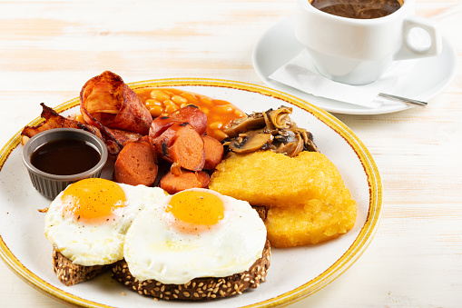 Fried eggs with sausages, nuggets, mushrooms and cup of coffee. Îreakfast concept.