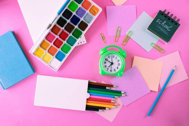 istock Back to school concept with colored pencils, stickers, alarm clock and notepad on pink background 1609654130
