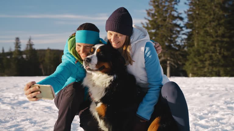 SLO MO Two women having fun taking selfies with their dog in the snowy terrain