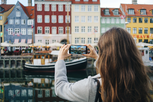 Woman taking pictures with smartphone in Copenhagen, Denmark. Nyhavn is one of the main landmark of Copenhagen.