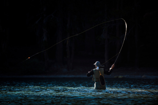 A fly fisherman wading in the middle of a river.