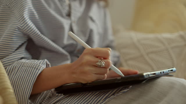 Hand of woman using digital tablet to learn while sitting on the sofa in the living room at home