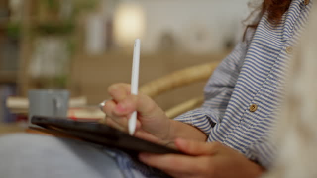 Hand of woman using digital tablet to learn while sitting on the sofa in the living room at home