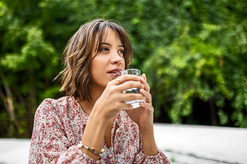 Beautiful woman sitting at the terrace on a sunny day drinking a fresh glass of water