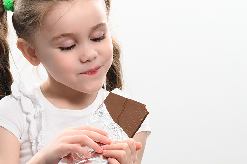 A happy and smiling little girl has a chocolate bar, portrait of a child with chocolate on a white background, baby teeth and chocolate.