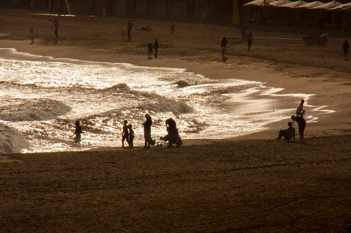 Barceloneta beach in Barcelona, Catalonia, Spain,  autumn afternoon at dusk with  silhouetted people walking on gold colored sand.
