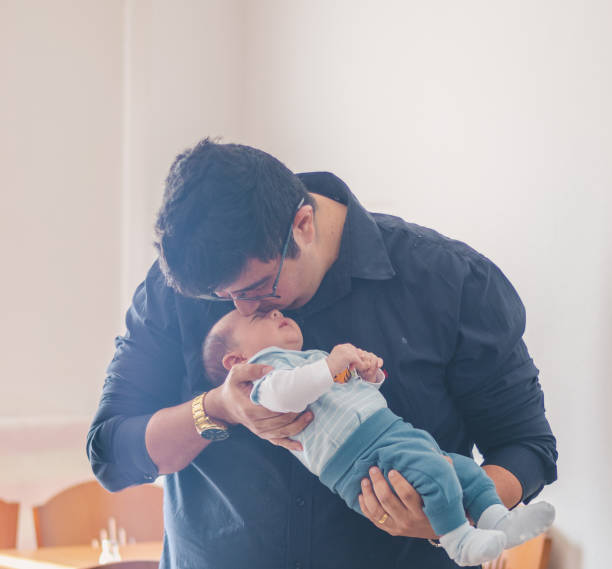 Dad holding newborn baby in his arms, kissing him on the forehead