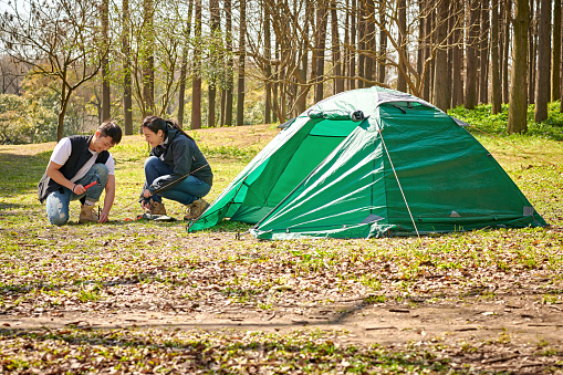 Asia man & woman putting-up tent at camping trip at sunset sunlight.