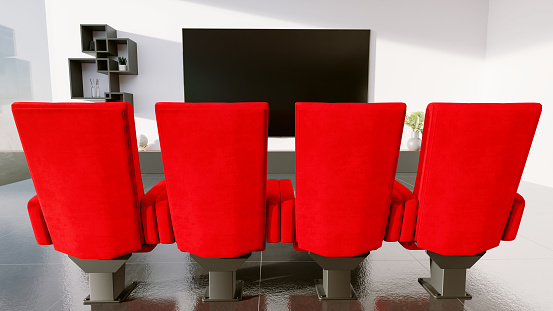 Red chairs like the ones from the cinema stand in a living room in front of a big flatscreen television. Concept of home cinema and streaming movies from your house and having an immersive experience.
