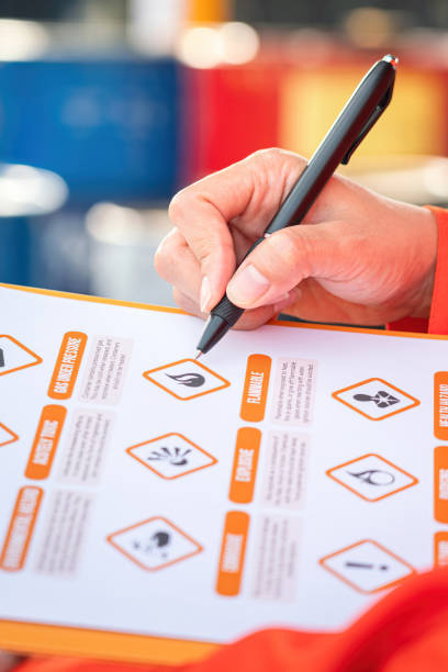 Checking on the chemical hazardous material form. Industrial safety working. Action of safety officer is using a pen to checking on the hazadous material symbol label form with the chemical barrel as blurred background. Safety industrial working scene concept. Selective focus. occupational safety and health stock pictures, royalty-free photos & images