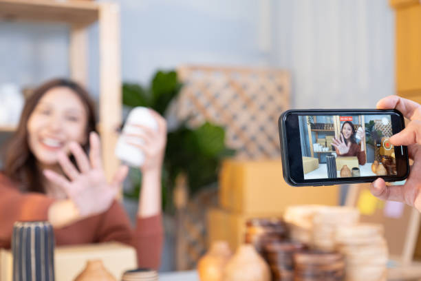 istock Selective focus at smartphone, Young Asian female entrepreneur smile while talking on the phone and check customer order from online shopping inside of home office. New small business start up trend. 1609871369