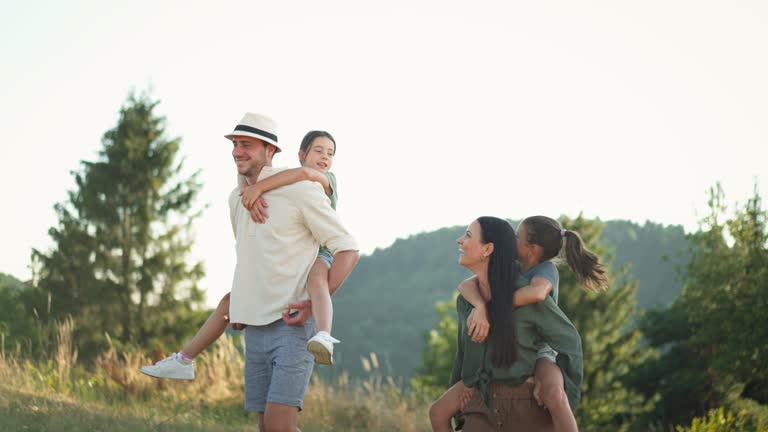 Happy parents giving their children piggyback ride in summer in nature.