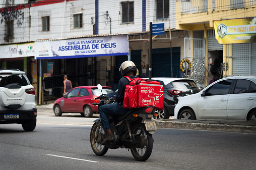 Salvador, Bahia, Brazil - August 11, 2023: A food delivery person using the ifood app is seen riding his motorcycle on Avenida Bonoco in Salvador, Bahia,