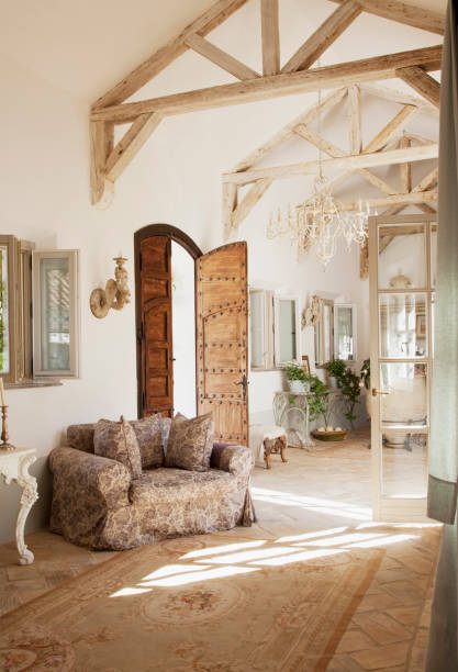 Wide angle view of living area with love seats, chairs, coffee table, and fireplace in traditional Spanish farmhouse featuring beamed ceiling and slate flooring.