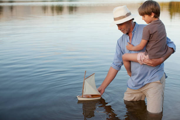 nonno e nipote di pesca sul lago con barca a vela giocattolo - sailing nautical vessel family lake foto e immagini stock