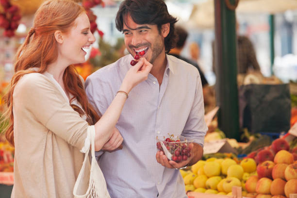 sonriente pareja de degustación de frutas en el mercado. - tasting women eating expressing positivity fotografías e imágenes de stock