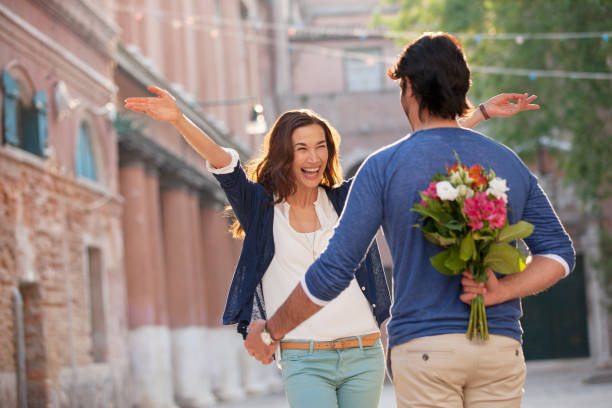 femme enthousiaste s'approcher homme avec des fleurs derrière le dos - sapprocher photos et images de collection