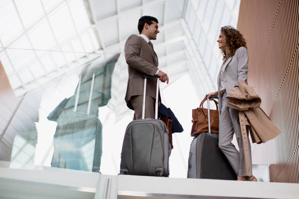 souriant homme d'affaires et femme d'affaires avec les valises parler à l'aéroport - business travel photos et images de collection