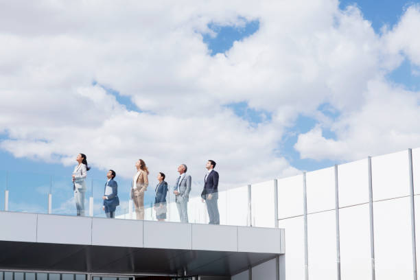 business people on rooftop balcony looking up at sky - anticipation 뉴스 사진 이미지