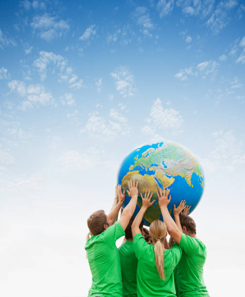 Team in green t-shirts lifting globe overhead  sustainable lifestyle photos stock pictures, royalty-free photos & images