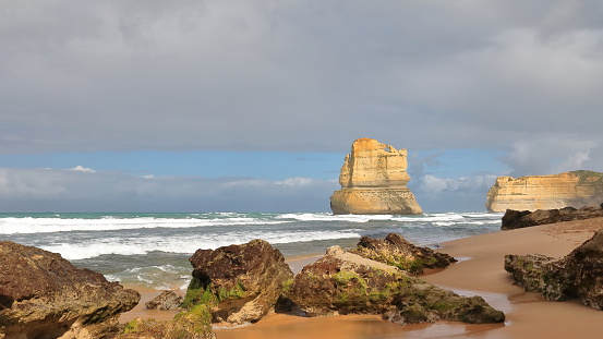 Westwards view from the beach at the Gibson Steps foot at low tide of Gog large sea stack hiding small Magog eroded from the Port Campbell Limestone, algae covered boulders on the sand. VIC-Australia.