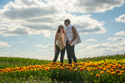 A beautiful young couple, fashion models stands in sportswear at the background of a field of colorful tulips. A guy looks at the girl.