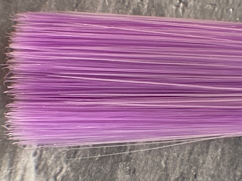 An extreme close up on a kids purple bristled paintbrush sitting on a grey marble countertop