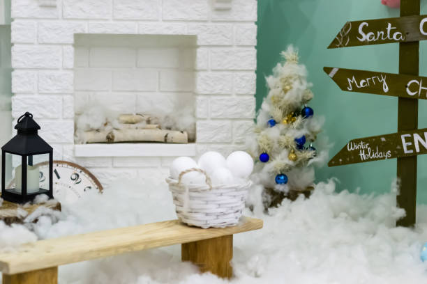 istock Winter New Year interior. Fireplace. lantern, bench, snow balls, Christmas tree with balls. Cozy decor in white tones in the interior of the Christmas room, a Christmas tree decorated with garlands, gifts. A festive living room in the house. New Year's h 1610045547