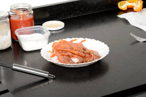 фотография креветок, приготовленных на белой тарелке, помещенных на столешницу из черного гранитного мрамора, рядом с несколькими банками, - prepared crustacean flash стоковые фото и изображения