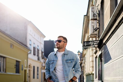 Young adult brunette adult wearing sunglasses and jeans jacket walks around the town.