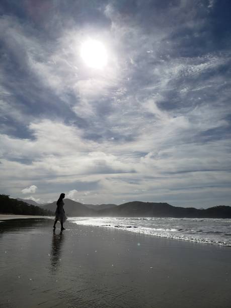 istock Woman walking on the beach with sunset in the background 1610149849