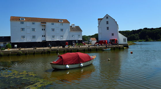 Woodbridge, Suffolk, England -  June 15, 2023: Woodbridge Quay and Tide Mill with boat on the river Deben.
