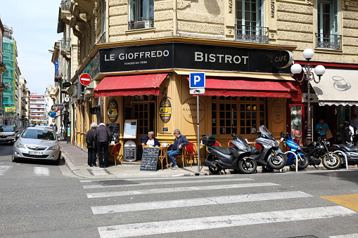 Nice, France - April 22, 2023: At the intersection of the streets, on the corner of the building, there is a restaurant and sidewalk cafe whose seats are now taken