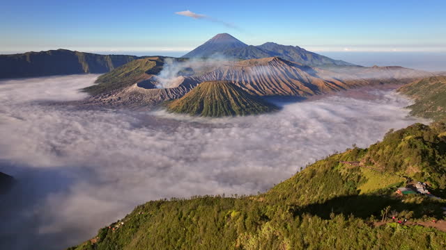 Drone aerial view fly backward and tilt up to reveal Bromo volcano in a background, East Java, Indonesia