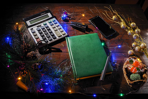 Work diary on the table. Festive mood. Christmas garlands and decorations. Calculator and smartphone on the table. Top view at an angle.